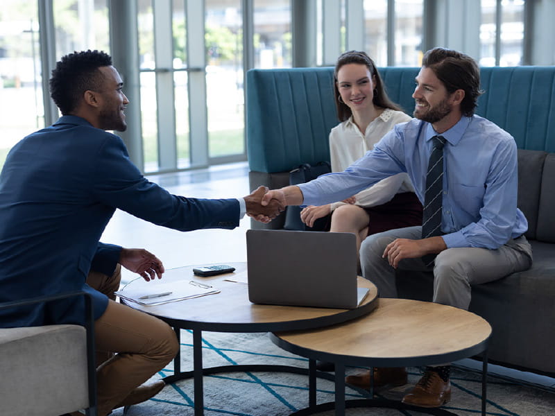 financial-negotiation-success-couple-feature A professional advisor shaking hands with a happy couple after successfully navigating a complex financial matter.