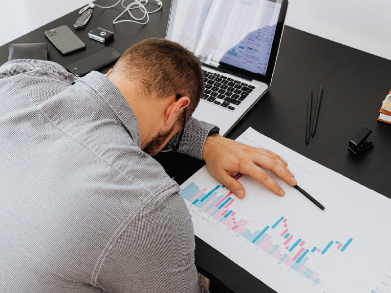 overcoming-financial-stress-overwhelmed-owner-feature A stressed man surrounded by disorganised paperwork and laptop, representing the need for financial coordination.